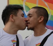 A queer or gay couple sharing a kiss in front of an LGBTQ Pride flag