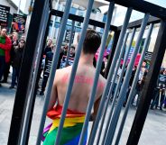 An activist stands naked, wrapped in a rainbow flag, in a mock cage in front of the Chancellery in Berlin on April 30, 2017, during a demonstration calling on Russian President to put an end to the persecution of gay men in Chechnya.