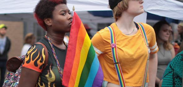 A black woman holding a rainbow flag next to a white woman wearing rainbow braces