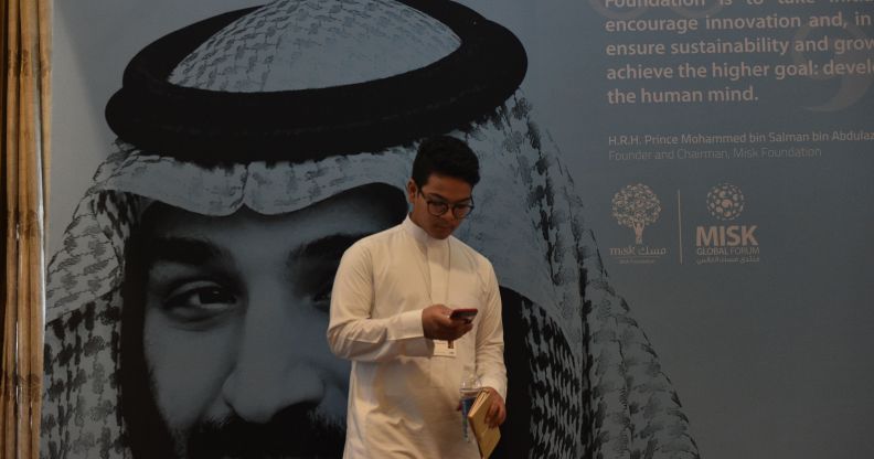 A young man in Saudi Arabia, where textbooks teach gay sex is punishable by death, stands in front of a portrait of Saudi Crown Prince Mohammed bin Salman.