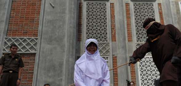 TOPSHOT - A religious officer canes an Acehnese youth onstage as punishment for dating outside of marriage, which is against sharia law, outside a mosque in Banda Aceh on August 1, 2016. The strictly Muslim province, Aceh has become increasingly conservative in recent years and is the only one in Indonesia implementing Sharia law. / AFP / CHAIDEER MAHYUDDIN (Photo credit should read CHAIDEER MAHYUDDIN/AFP/Getty Images)