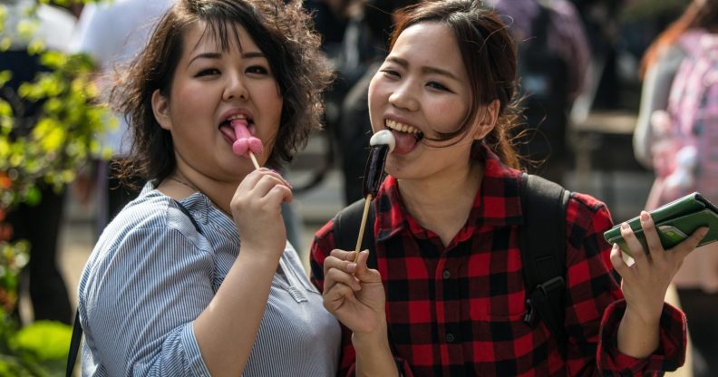 KAWASAKI, JAPAN - APRIL 01: (EDITORS NOTE: Image contains suggestive content.) Women react to the camera as they eat phallic-shaped lollipops during Kanamara Matsuri (Festival of the Steel Phallus) on April 1, 2018 in Kawasaki, Japan. The Kanamara Festival is held annually on the first Sunday of April. The penis is the central theme of the festival, focused at the local penis-venerating shrine which was once frequented by prostitutes who came to pray for business prosperity and protection against sexually transmitted diseases. Today the festival has become a popular tourist attraction and is used to raise money for HIV awareness and research. (Photo by Carl Court/Getty Images)