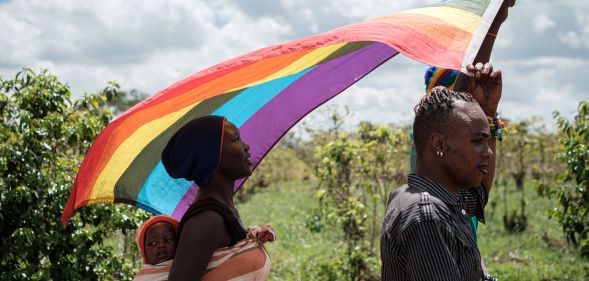 Two LGBT+ refugees and a child march holding a rainbow flag