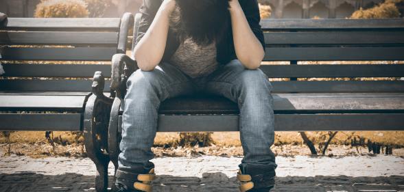 Boy holds his head in his hands as he sits on a bench