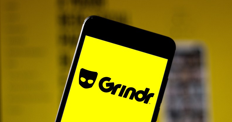 A phone showing a yellow screen with the Grindr logo