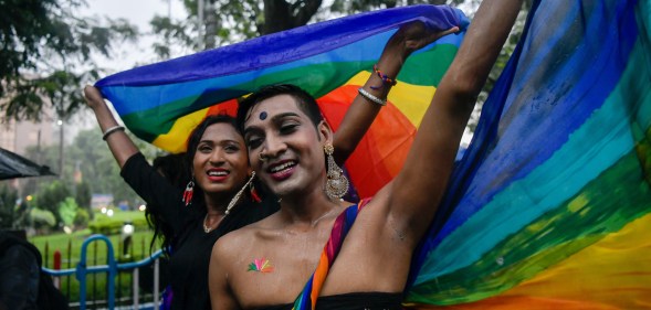 Two smiling people hold a rainbow flag