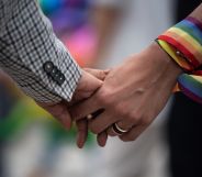 A close-up of a same-sex couple holding hands, one has a rainbow ribbon wrapped around their wrist