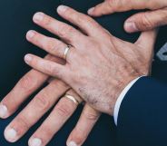 Two male hands touching, both wearing wedding rings