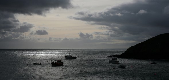 View out to sea from Creux Harbour on Sark, showing fishing boats in silhouette on a grey sea with a cloudy grey sky, 21st November 2008