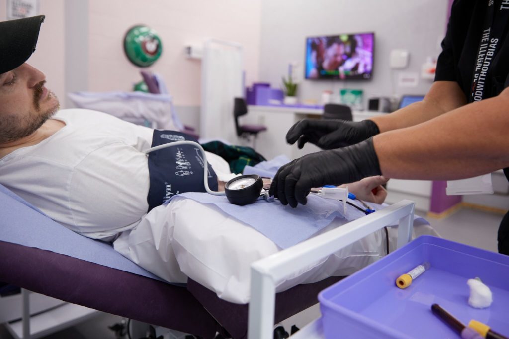 A medic preps a queer man to donate blood. (UNILAD)