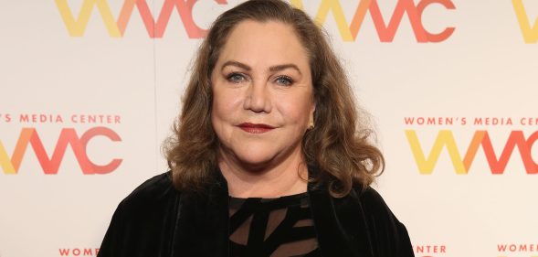 A photo shows actor Kathleen Turner wearing a black dress and smiling at the camera during a press event at the Women's Media Awards