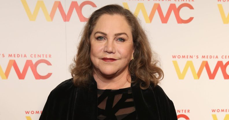 A photo shows actor Kathleen Turner wearing a black dress and smiling at the camera during a press event at the Women's Media Awards