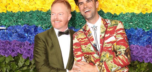 Modern Family Jesse Tyler Ferguson and his husband Justin Mikita in front of a rainbow flower wall