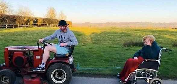 Tommy Ferris tows his grandmother's wheelchair on his sit-down lawnmower. (Screen capture via BBC)