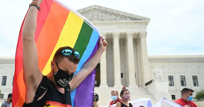 A man waves a rainbow flag in front of the Supreme Court.