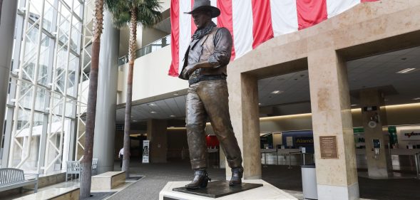 A statue of John Wayne is on display beneath an American flag in John Wayne Airport, located in Orange County, on June 28, 2020 in Santa Ana, California. Orange County