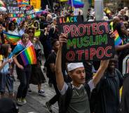 Man holding a 'protect Muslim QTIPOC' placard in a Pride parade