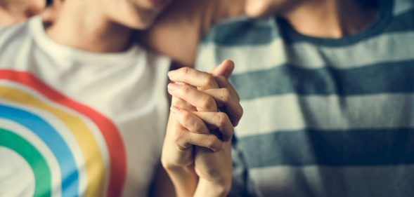 Lesbian couple holding hands, one wearing a rainbow t-shirt and another in a green striped top