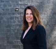 Photo of Conservative MP Caroline Nokes wearing a black suit standing in front of a grey brick wall