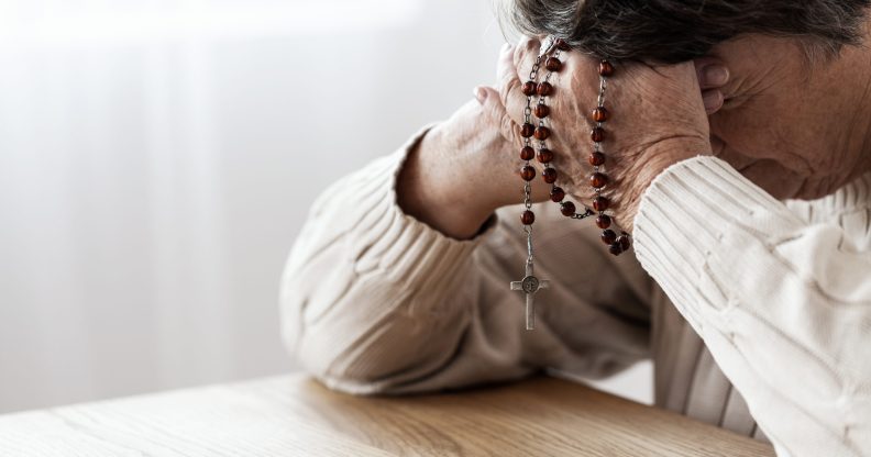 A man clutching rosary beads to his head