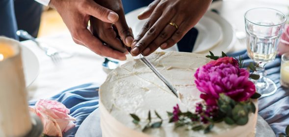 Close-up of two male hands cutting a wedding cake