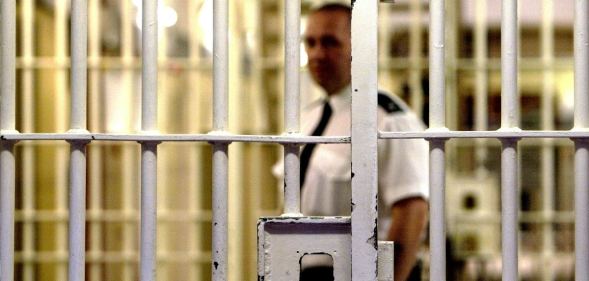 Stock photograph of a prison warden outside jail cell bars