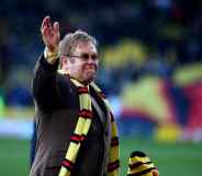 Elton John wearing a Watford FC scarf on a football pitch