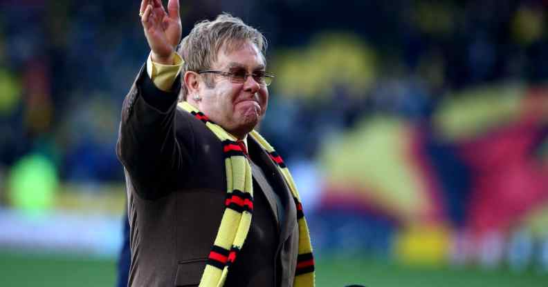 Elton John wearing a Watford FC scarf on a football pitch