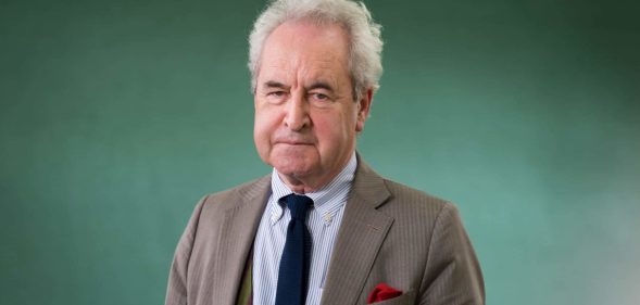 John Banville wearing a suit and tie against a green backdrop