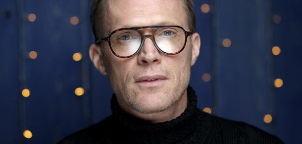 Paul Bettany looking into the camera wearing glasses and a black turtleneck