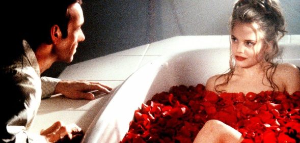 Kevin Spacey leering over a naked young woman in a bath filled with flowers