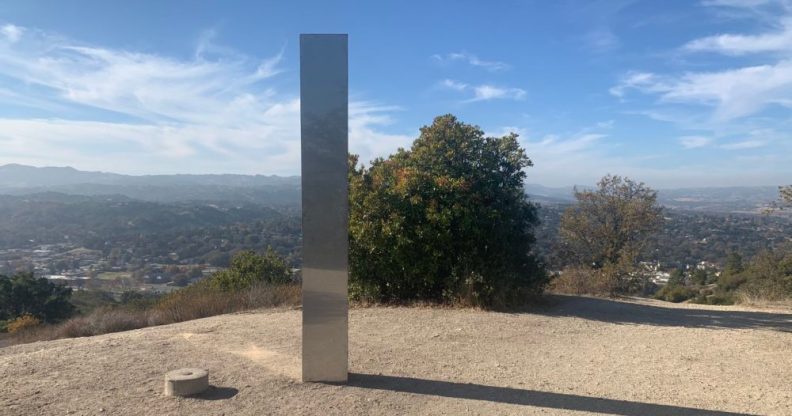 A tall, slim silver monolith at the top of an empty hill