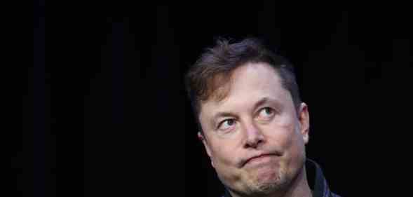 Elon Musk shrugs against a black background during a conference