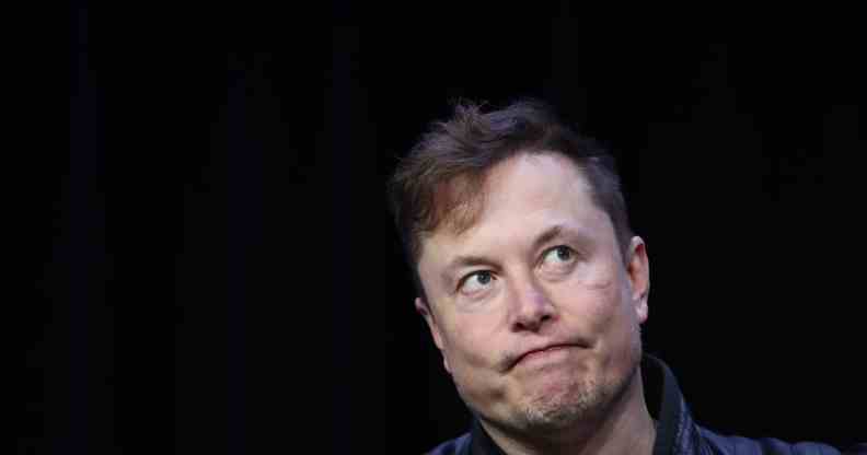 Elon Musk shrugs against a black background during a conference
