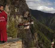 A monk stands on the mountaintops, a monastery in view behind him on the cliffs