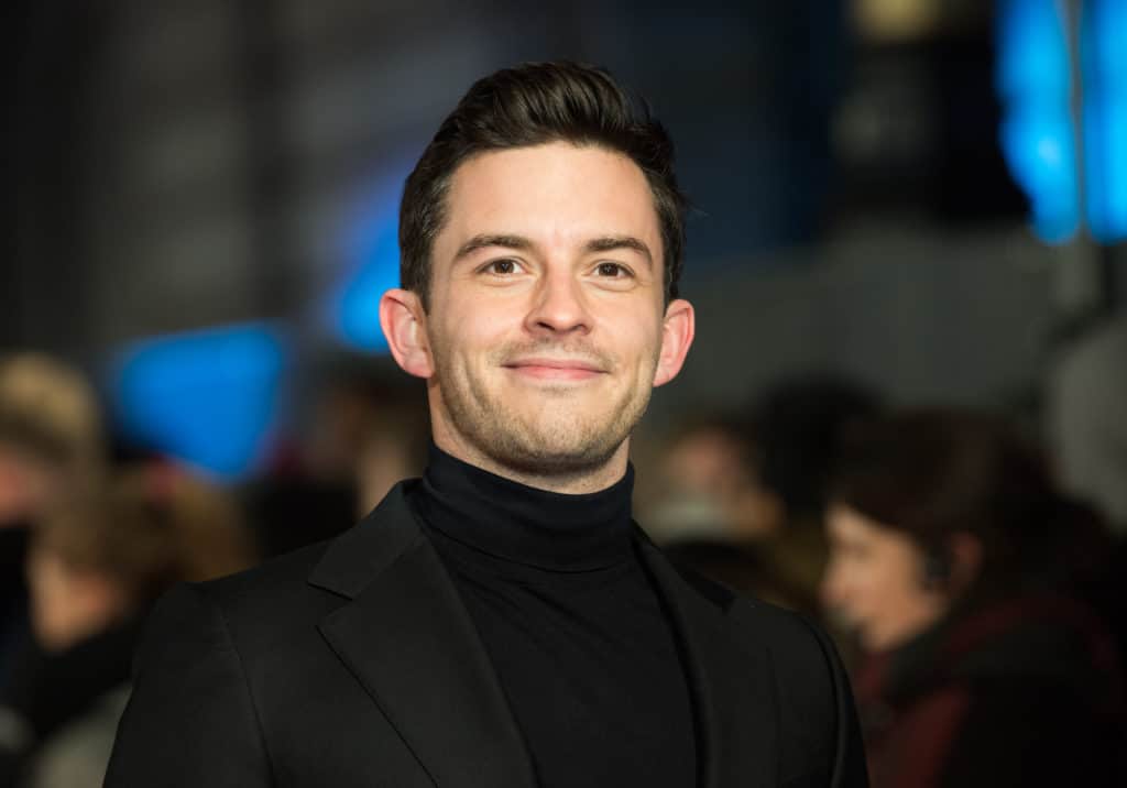 Jonathan Bailey smiles while wearing a black turtleneck and blazer