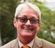 Carmen Vázquez smiles in a beige suit, white shirt and orange tie