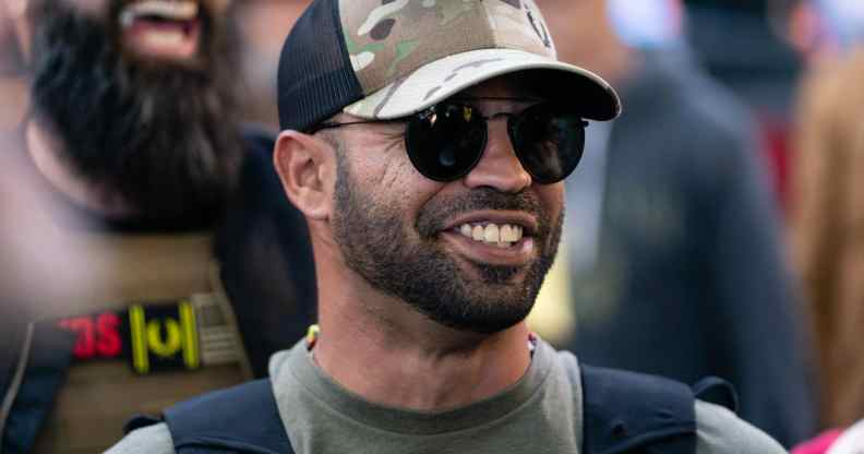 Proud Boy leader Enrique Tarrio smile while wearing a dark green t-shirt and cap