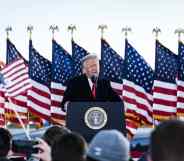 President Donald Trump speaks to his supporters on stage, American flags behind him