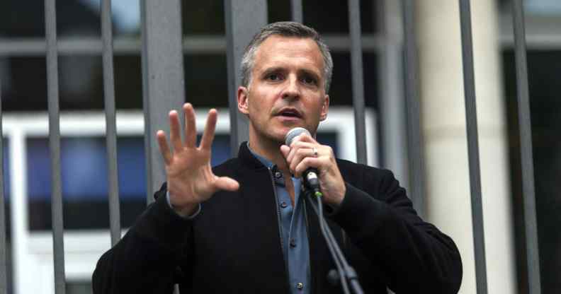 Rufus Gifford speaks into a microphone in a blue shirt and dark blazer