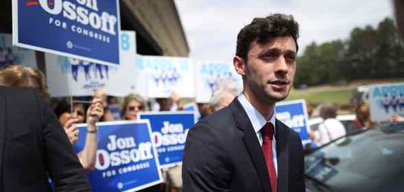 Jon Ossoff in a suit speaks to reporters while supporters hold up signs