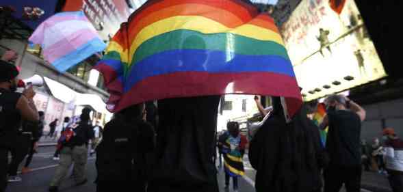 Americans holding a pride flag and trans flag in the background during a protest.