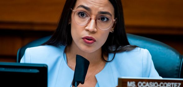 Alexandria Ocasio-Cortez in a blue suit speaking into a microphone in congress