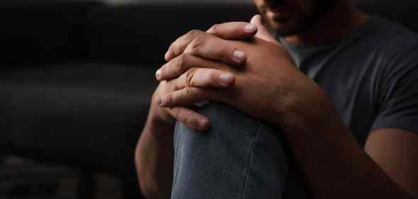 A sad man sitting on floor at home, his hands on his knee