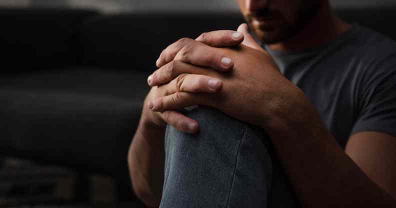 A sad man sitting on floor at home, his hands on his knee