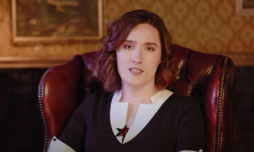 Abigail Thorn sitting on a leather chair wearing a white shiny and black v-neck jumper