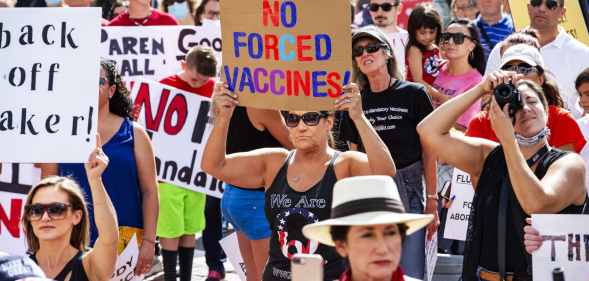 A woman with a QAnon shirt stands among an anti-vaccination protes