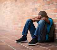 Young boy with his head in his harms leaning against a brick wall