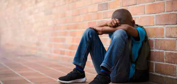 Young boy with his head in his harms leaning against a brick wall