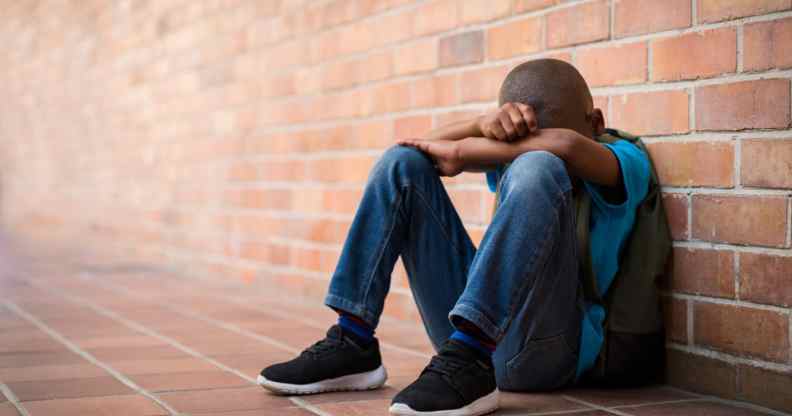 Young boy with his head in his harms leaning against a brick wall